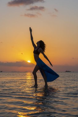 Gün batımında, Tayland 'daki cennet adasında tropikal sahilde dans eden genç bir kız. Yaz kavramı. Tatil seyahati.