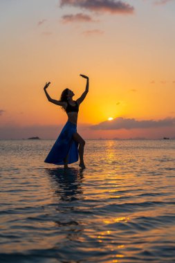 Gün batımında, Tayland 'daki cennet adasında tropikal sahilde dans eden genç bir kız. Yaz kavramı. Tatil seyahati.