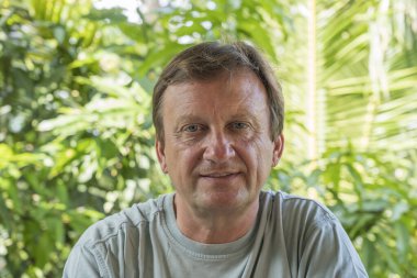 Yeşil yapraklı arka planda dinlenen orta yaşlı bir adamın portresi.