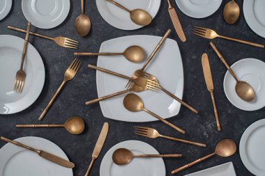 Siyah arka planda bir sürü beyaz seramik tabak, pirinç çatal, bıçak ve kaşık var. Üst görünüm, kapat