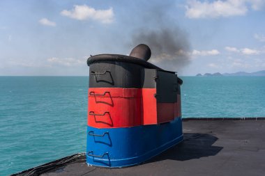 Denizdeyken feribot bacasından duman, güneş ışığı, deniz suyu ve arka planda mavi gökyüzü, Tayland. Gemide, bir feribot ya da yolcu gemisinin bacasında bacalar atmosferi kirletir.