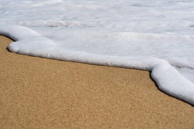Güneşli bir günde, kumlu sahilde, beyaz, temiz köpükle denizin yumuşak dalgası. Doğa konsepti