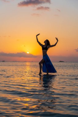Gün batımında, Tayland 'daki cennet adasında tropikal sahilde dans eden genç bir kız. Yaz kavramı. Tatil seyahati.