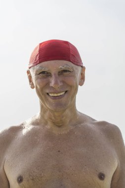 Deniz suyunun yanındaki kumsalda kırmızı yüzme şapkalı mutlu yaşlı adam, yaklaş.