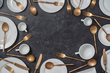 Birçok beyaz seramik tabak, fincanlar ve pirinç çatallar, siyah arka planda bıçaklar ve kaşıklar ve metin için kopyalama alanı. Üst görünüm, kapat