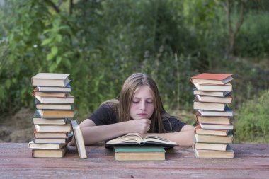 Bahçede, tahta bir masada kitap yığınıyla kitap okuyan genç bir kız. Ev eğitimi kavramı