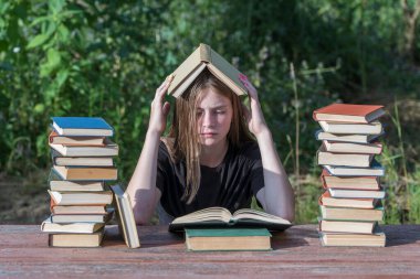 Bahçede, tahta bir masada kitap yığınıyla kitap okuyan genç bir kız. Ev eğitimi kavramı