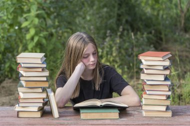 Bahçede, tahta bir masada kitap yığınıyla kitap okuyan genç bir kız. Ev eğitimi kavramı