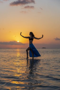 Gün batımında, Tayland 'daki cennet adasında tropikal sahilde dans eden genç bir kız. Yaz kavramı. Tatil seyahati.