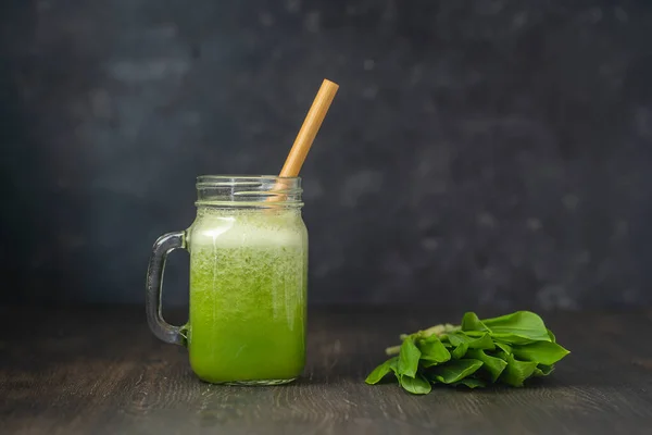 Glass mug of green juice smoothie shake from ramson, banana and honey on a black background, close up. Healthy eating, food, dieting and vegetarian concept. Raw drink from wild garlic and banana