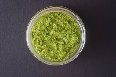 Siyah arka planda izole edilmiş cam bir kasede yeşil pesto sosu, yakın plan, üst manzara. Vahşi sarımsak, çam fıstığı, tuz ve biberden yapılmış taze pesto sosu.