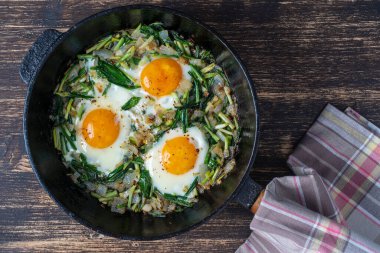 Shakshuka, yeşil sarımsak yapraklı sahanda yumurta, soğan, biber ve baharat dökme demir tavada, yakın çekim. Shakuka gibi yabani sarımsaklı sahanda yumurta