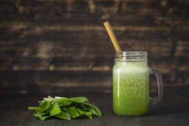 Ramson 'dan bir bardak yeşil meyve suyu kokteyli, ahşap arka planda muz ve bal, yakın plan. Sağlıklı beslenme, yemek, diyet ve vejetaryen konsepti. Yabani sarımsak ve muzdan çiğ içecek.