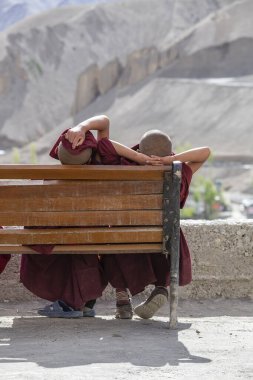Güneşli bir günde, Ladakh, Kuzey Hindistan 'daki dağ manastırı Lamayuru' nun yanındaki bankta dinlenen iki genç Budist keşiş.