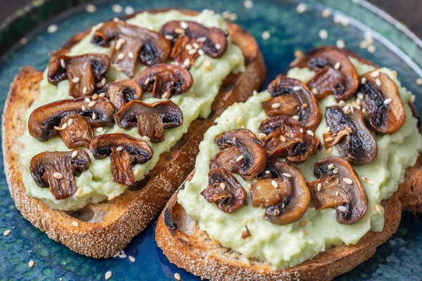 Вкусный сэндвич с зеленым пюре авокадо, жареные грибы и семена кунжута в тарелке на столе, закрывайте. Вегетарианская еда