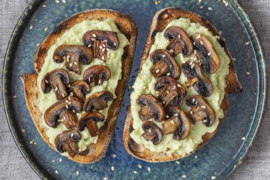 Lezzetli sandviç, yeşil püre avokado, kızarmış mantar ve masada susam tohumu, yakın çekim. Vejetaryen yemeği.