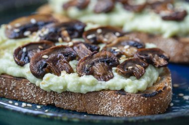 Lezzetli sandviç, yeşil püre avokado, kızarmış mantar ve masada susam tohumu, yakın çekim. Vejetaryen yemeği.