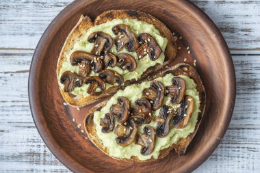 Lezzetli sandviç, yeşil püre avokado, kızarmış mantar ve masada susam tohumu, yakın çekim. Vejetaryen yemeği.