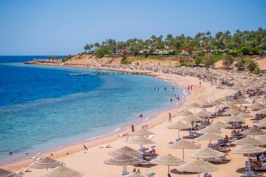 Sharm El Sheikh, Mısır - 28 Mayıs 2021: İnsanlar Sharm El Sheikh, Mısır, Afrika 'daki Kızıldeniz kıyısındaki bir tropik tatil beldesinde plaj sandalyeleri ve saman şemsiyeleriyle lüks bir kumsalda dinleniyorlar.