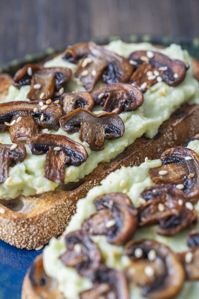 Tasty sandwich with green mashed avocado, fried mushrooms and sesame seeds in plate on a table, close up. Vegetarian food