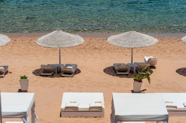 Mısır, Afrika 'daki Kızıldeniz kıyısındaki tropikal tatil beldesinde plaj sandalyeleri ve beyaz saman şemsiyeleriyle lüks kumsal. Karantina sırasında boş plajlar