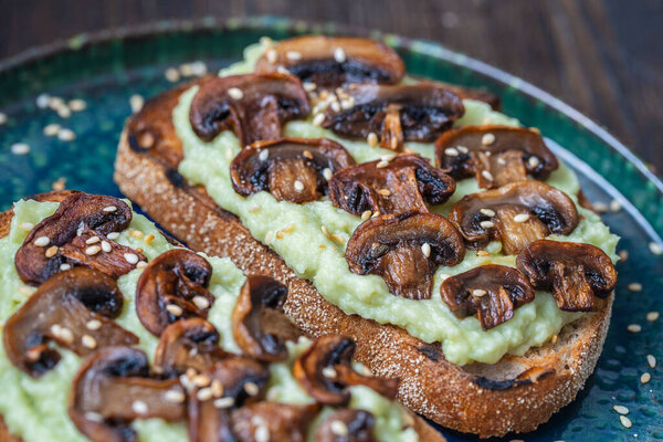 Tasty sandwich with green mashed avocado, fried mushrooms and sesame seeds in plate on a table, close up. Vegetarian food
