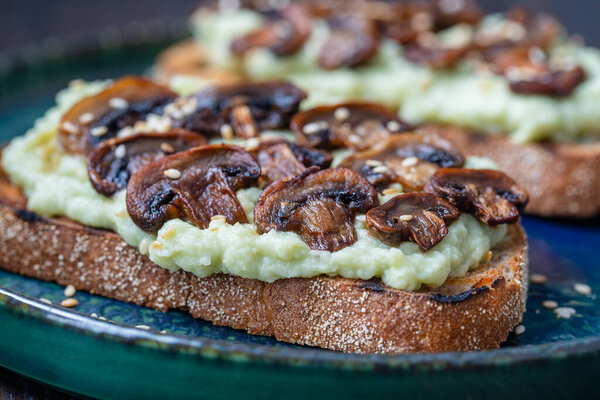 Tasty sandwich with green mashed avocado, fried mushrooms and sesame seeds in plate on a table, close up. Vegetarian food
