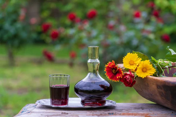木製のテーブルの上に夏の庭の背景に花の花びらで飾られた赤ワインとガラスのデカンタとガラス クローズアップ — ストック写真