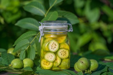 Dilimlenmemiş cevizleri bir kavanozda alkolle, ev yapımı tentür hazırlamak için, yakın çekim. Bahçedeki bir masada cam kavanozda yeşil ceviz tentürü.