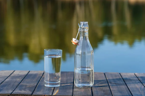 Glas Och Flaska Med Dricksvatten Ett Träbord Morgonen Nära Sjön — Stockfoto