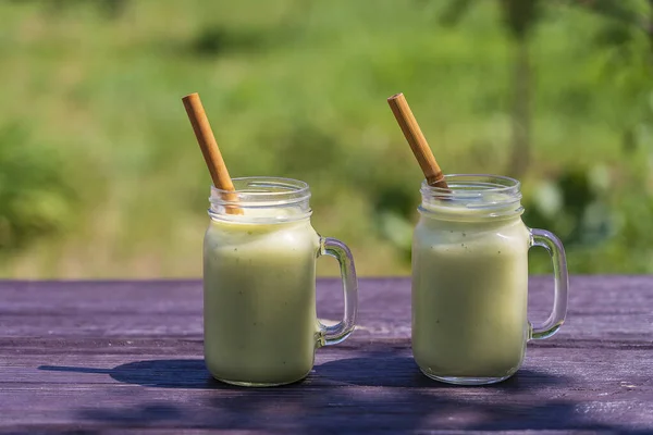新鲜的绿色冰沙从鳄梨 香蕉和蜂蜜玻璃杯子在木制桌子上的自然背景 健康饮食的概念 在阳光明媚的夏日 花园里的绿色冰沙 — 图库照片