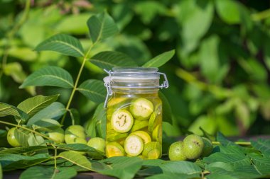 Dilimlenmemiş cevizleri bir kavanozda alkolle, ev yapımı tentür hazırlamak için, yakın çekim. Bahçedeki bir masada cam kavanozda yeşil ceviz tentürü.