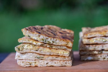 Ahşap bir masanın üzerinde süzme peynir ve otlarla pişirilmiş hamur tortilla parçaları, yakın çekim, geleneksel Türk yemeği.