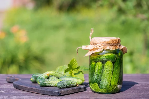 Taze ve tuzlu, cam bir kavanozda salatalık turşusu, güneşli bir günde yaz bahçesindeki eski bir ahşap masada, kopyalama alanı, kapat. Yeşil salatalıklı kavanoz, otlar, dereotu, sarımsak