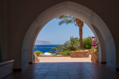 Mısır, Afrika 'daki Sharm El Sheikh tatil köyünde, Kızıl Deniz kıyısındaki bir binanın güzel kemerli kapısı. Mavi deniz, yeşil palmiye ağacı ve kumsalda kemer.