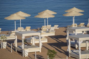 Mısır, Afrika 'daki Kızıldeniz kıyısındaki tropikal tatil beldesinde plaj sandalyeleri ve beyaz saman şemsiyeleriyle lüks kumsal. Karantina sırasında boş plajlar