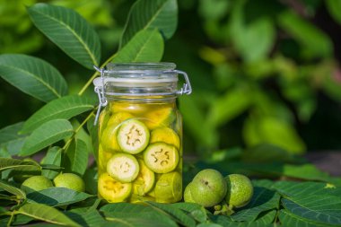 Dilimlenmemiş cevizleri bir kavanozda alkolle, ev yapımı tentür hazırlamak için, yakın çekim. Bahçedeki bir masada cam kavanozda yeşil ceviz tentürü.