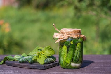 Taze ve tuzlu, cam bir kavanozda salatalık turşusu, güneşli bir günde yaz bahçesindeki eski bir ahşap masada, kopyalama alanı, kapat. Yeşil salatalıklı kavanoz, otlar, dereotu, sarımsak