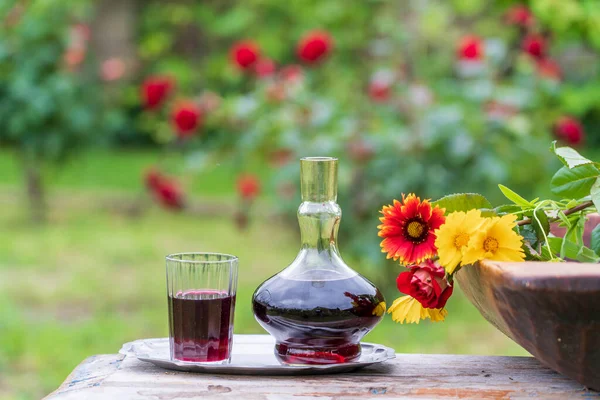 木製のテーブルの上に夏の庭の背景に花の花びらで飾られた赤ワインとガラスのデカンタとガラス クローズアップ — ストック写真