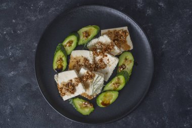 Yeşil salatalı taze salata ve zeytin yağı soslu beyaz peynir ve siyah tabakta kavrulmuş badem.