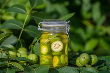 Dilimlenmemiş cevizleri bir kavanozda alkolle, ev yapımı tentür hazırlamak için, yakın çekim. Bahçedeki bir masada cam kavanozda yeşil ceviz tentürü.