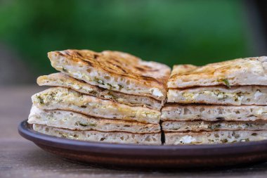 Ahşap bir masanın üzerinde süzme peynir ve otlarla pişirilmiş hamur tortilla parçaları, yakın çekim, geleneksel Türk yemeği.