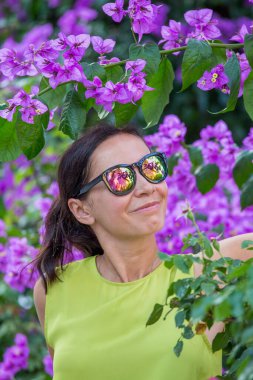 Güzel esmer kadının yaz portresi. Muhteşem mavi çiçek ağacı arka planında poz veriyor.