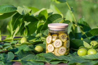 Dilimlenmemiş cevizleri bir kavanozda alkolle, ev yapımı tentür hazırlamak için, yakın çekim. Bahçedeki bir masada cam kavanozda yeşil ceviz tentürü.