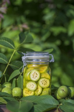 Dilimlenmemiş cevizleri bir kavanozda alkolle, ev yapımı tentür hazırlamak için, yakın çekim. Bahçedeki bir masada cam kavanozda yeşil ceviz tentürü.