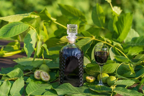 Liqueur from young green walnuts, remedy for stomach ache, close up. Tincture of green walnuts in a glass bottle on a table in the garden