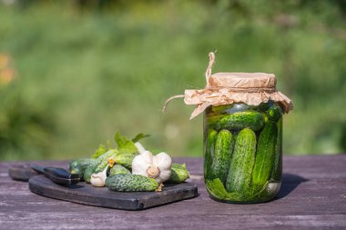 Taze ve tuzlu, cam bir kavanozda salatalık turşusu, güneşli bir günde yaz bahçesindeki eski bir ahşap masada, kopyalama alanı, kapat. Yeşil salatalıklı kavanoz, otlar, dereotu, sarımsak