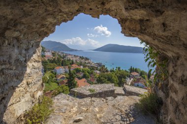 Herceg Novi şehri, mavi deniz ve Karadağ 'daki kalenin taş duvarındaki delikten geçen binalar. Güzel Kotor Körfezi ya da Boka Kotorska Körfezi girişinde yer alan kasaba.