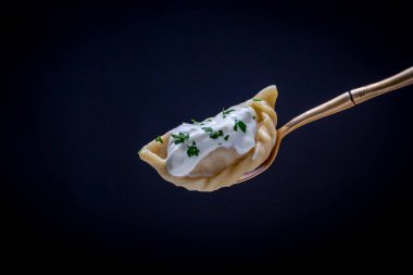 Ukrayna ve Rus yemekleri - Vareniki veya patates püresi ya da süzme peynirli hamur tatlısı, siyah arka planda çatallı ekşi krema ve maydanoz, yakın plan