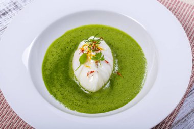 Beyaz tabakta haşlanmış yumurtalı yeşil sos.